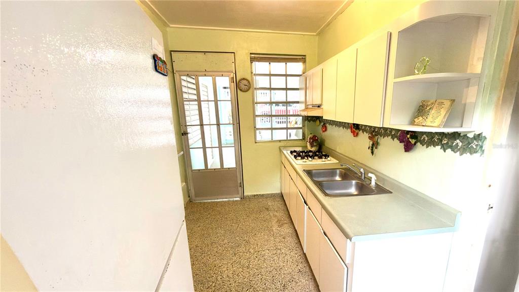 A galley-style kitchen features white cabinets, a double sink, a gas stove, and a door — . 123 KM 16.1 INT., PONCE, PR