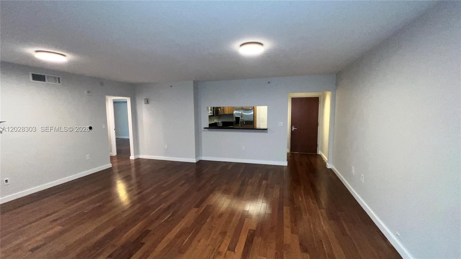 An empty living room features hardwood floors, light gray walls, and a kitchen pass-through window — 31 SE 5th St # 411, Miami FL 33131, MIAMI, FL