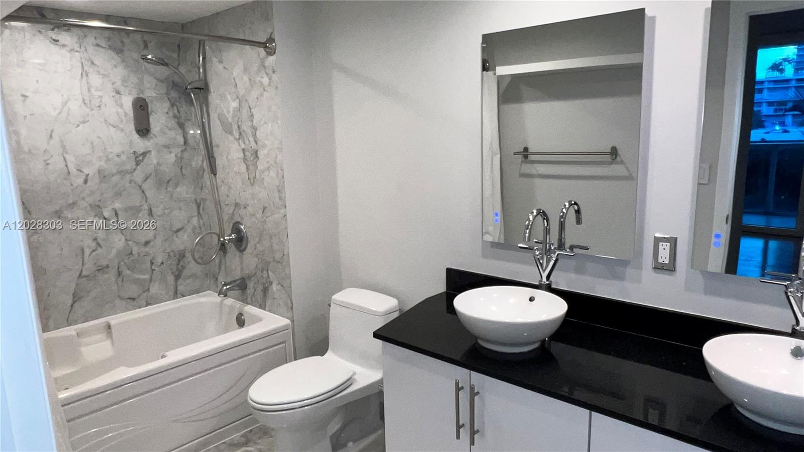 A bathroom features a marble-tiled shower, white vanity with dual vessel sinks, and black countertops — 31 SE 5th St # 411, Miami FL 33131, MIAMI, FL