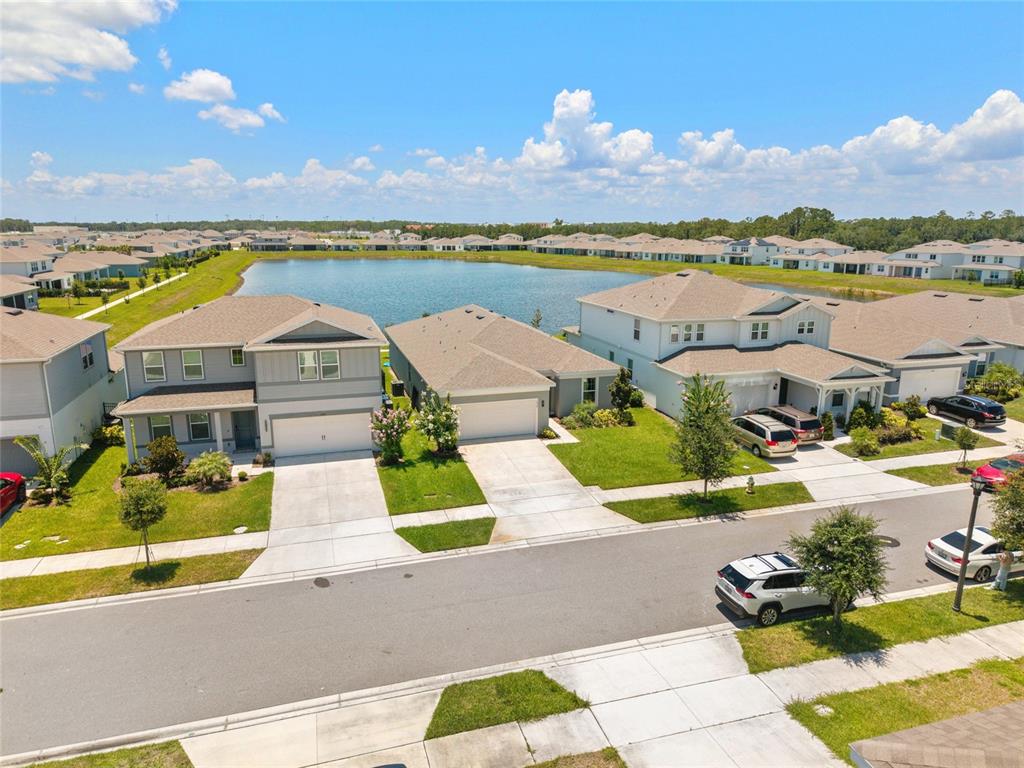 An aerial view shows suburban houses with garages and driveways bordering a large retention pond — 1634 GROVELINE RD, ST CLOUD, FL