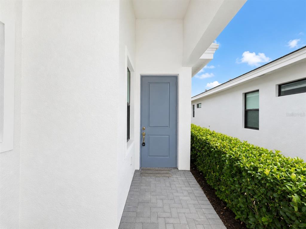 A blue front door opens onto a gray paver walkway beside a green hedge — 5182 BARNETT CIRCLE, LAKEWOOD RANCH, FL