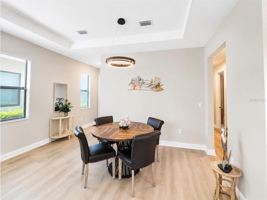 A dining area features a round wooden table, four dark chairs, and a modern pendant light — 5182 BARNETT CIRCLE, LAKEWOOD RANCH, FL