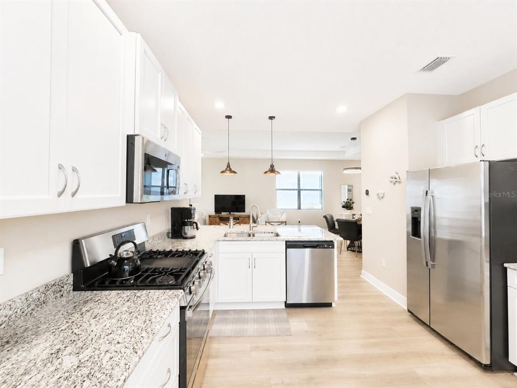 A kitchen with white cabinets, stainless steel appliances, and granite countertops opens to a living area — 5182 BARNETT CIRCLE, LAKEWOOD RANCH, FL