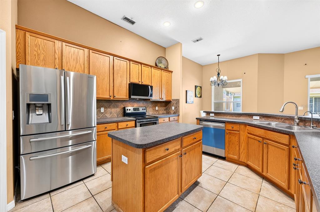 A kitchen with oak cabinets, stainless steel appliances, a center island, and tile flooring — 13537 KITTY FORK ROAD, ORLANDO, FL