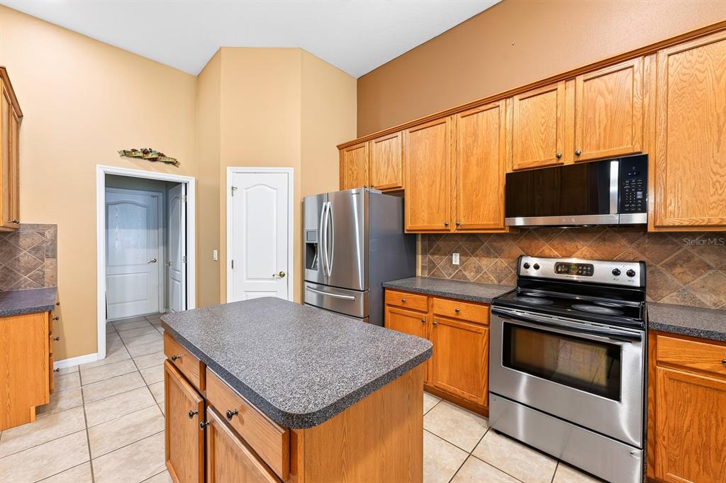 A kitchen features oak cabinets, stainless steel appliances, a center island, and tiled flooring — 13537 KITTY FORK ROAD, ORLANDO, FL