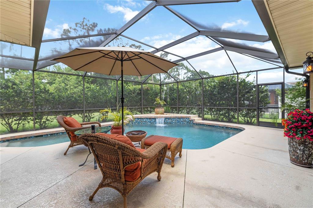 A screened-in patio features a swimming pool with a waterfall and wicker patio furniture — 13720 18TH PLACE E, BRADENTON, FL