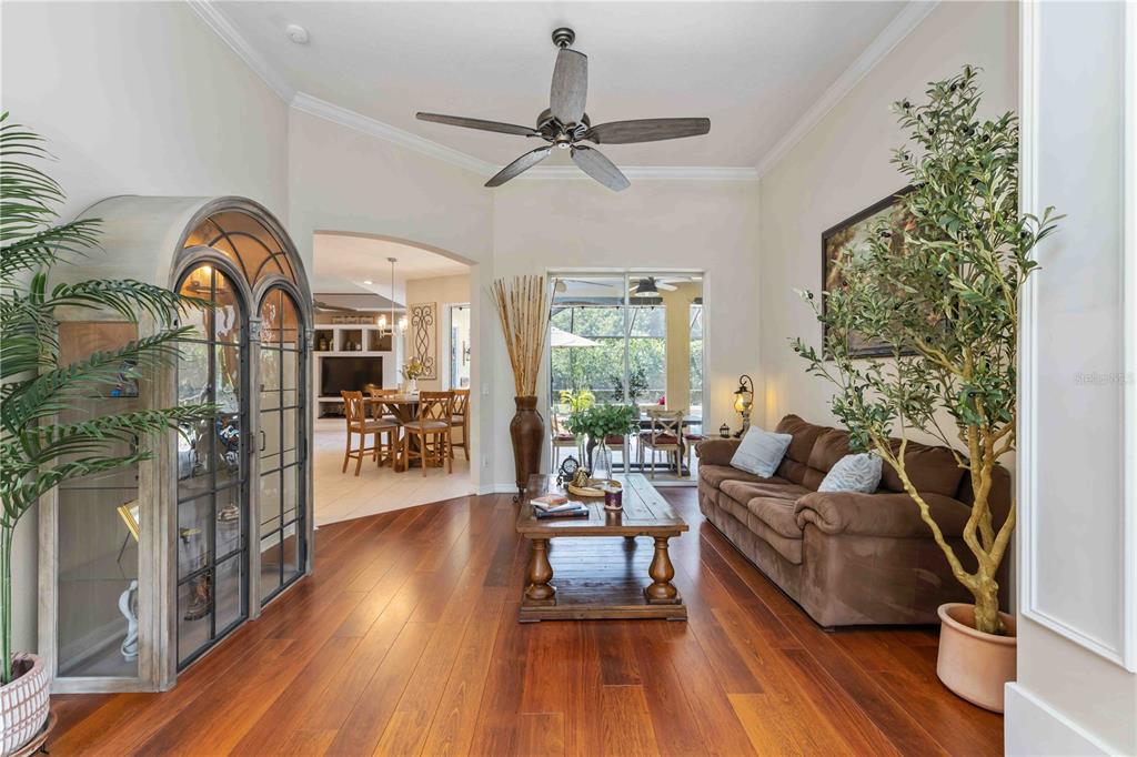 A living room with hardwood floors, a brown sofa, and a view into the dining area — 13720 18TH PLACE E, BRADENTON, FL