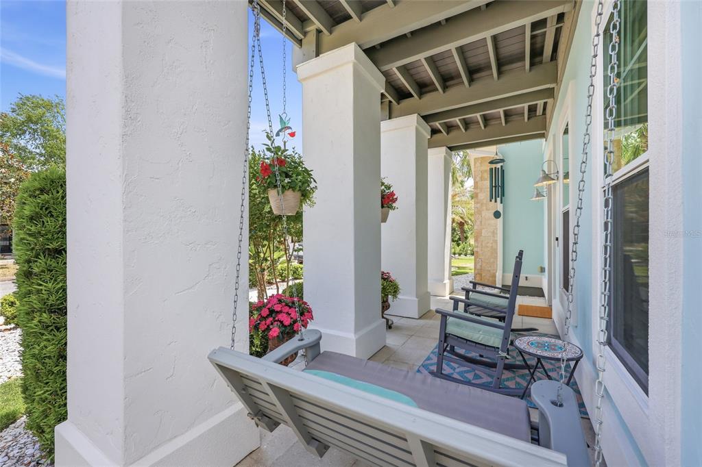 A covered porch features a hanging swing, two rocking chairs, and white stucco columns — 742 SW 132ND DRIVE, NEWBERRY, FL