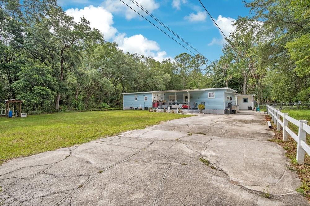 A light blue manufactured home with a front porch sits behind a large cracked driveway — 18222 LYNBROOK ROAD, ORLANDO, FL