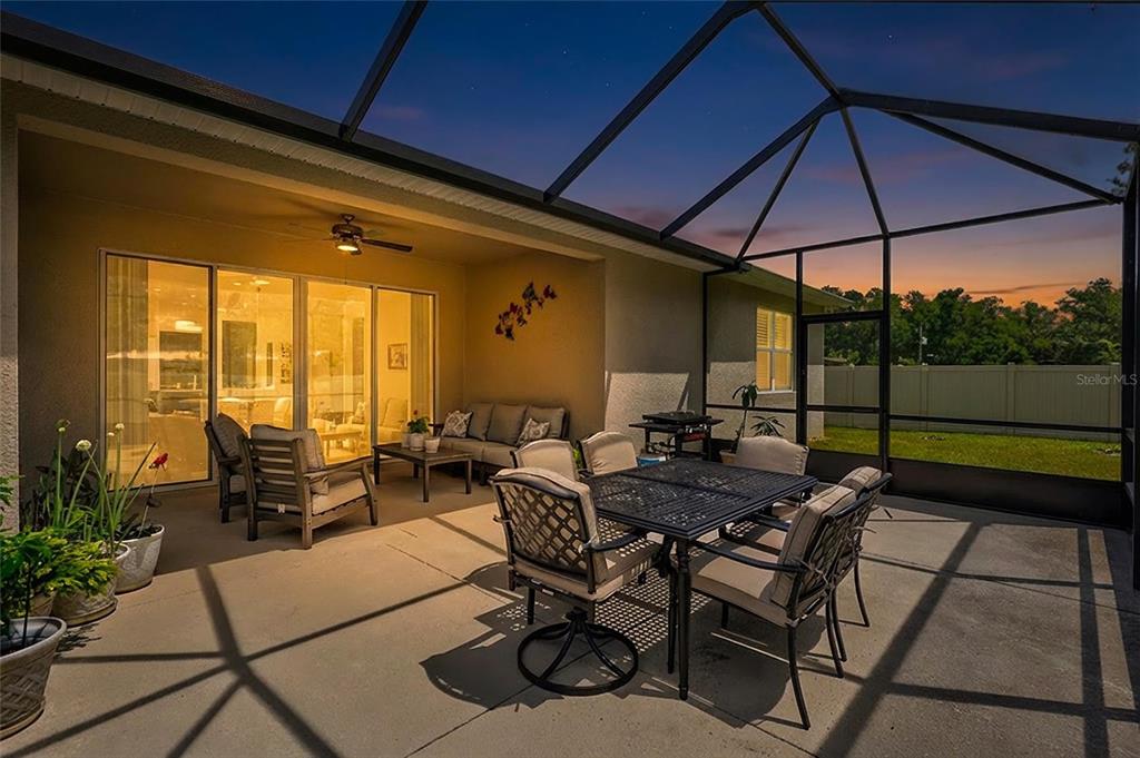 A screened-in patio features a dining set, lounge seating, and a ceiling fan at dusk — 6339 DOLOSTONE DRIVE, LAKELAND, FL
