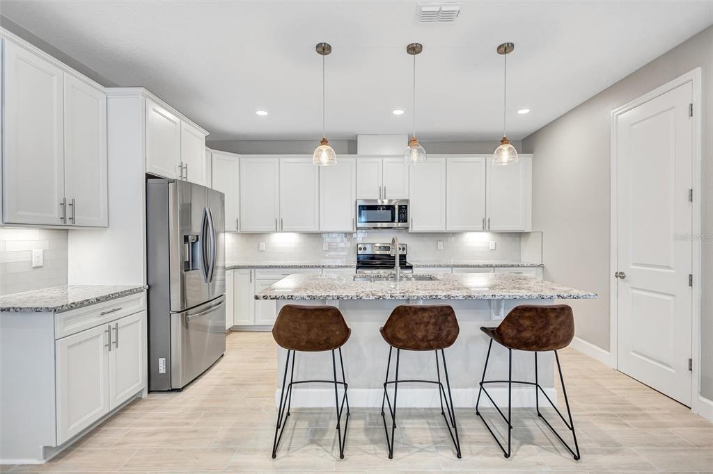 A modern kitchen features white cabinetry, granite countertops, a central island, and three bar stools — 6339 DOLOSTONE DRIVE, LAKELAND, FL