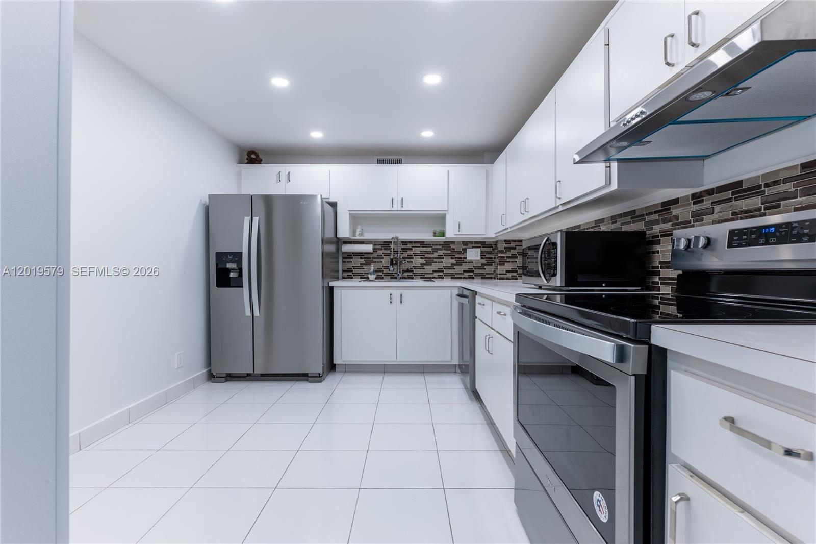 A modern kitchen features white cabinets, stainless steel appliances, and a tiled backsplash — 500 Three Islands Blvd # 1110, Hallandale Beach FL 33009, HALLANDALE BEACH, FL