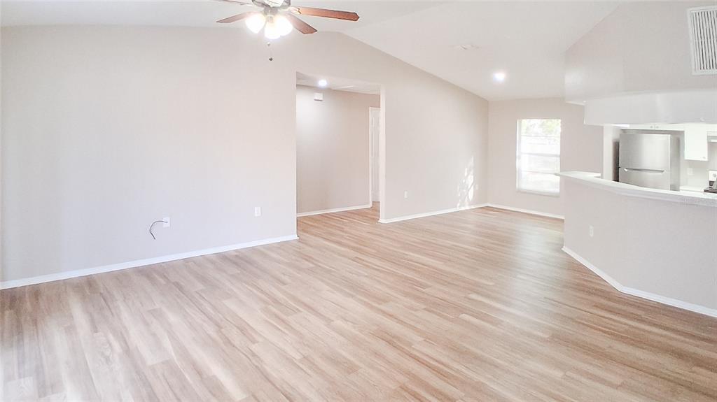 An open-concept living area features light wood-look flooring, neutral walls, and a ceiling fan — 4311 THONOTOSASSA AVENUE, TAMPA, FL