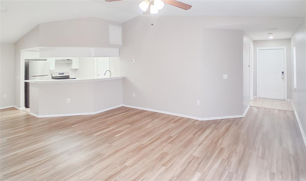An open-concept living area features light wood-look flooring, neutral walls, and a kitchen pass-through — 4311 THONOTOSASSA AVENUE, TAMPA, FL