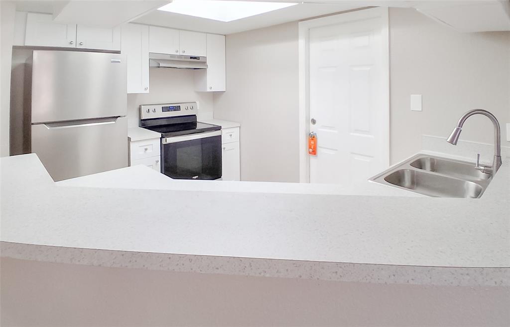 A kitchen features white cabinets, stainless steel appliances, and a white countertop breakfast bar — 4311 THONOTOSASSA AVENUE, TAMPA, FL