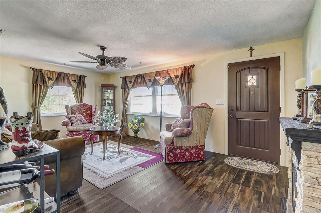 A living room features wood-look flooring, two floral armchairs, a brown door, and a ceiling fan — 298 POINCIANA AVENUE, PORT ORANGE, FL