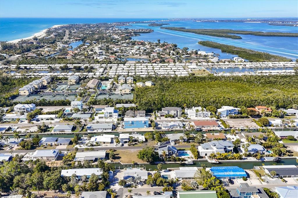 An aerial view shows a coastal neighborhood with houses, canals, and dense vegetation — 651 JUNGLE QUEEN WAY, LONGBOAT KEY, FL