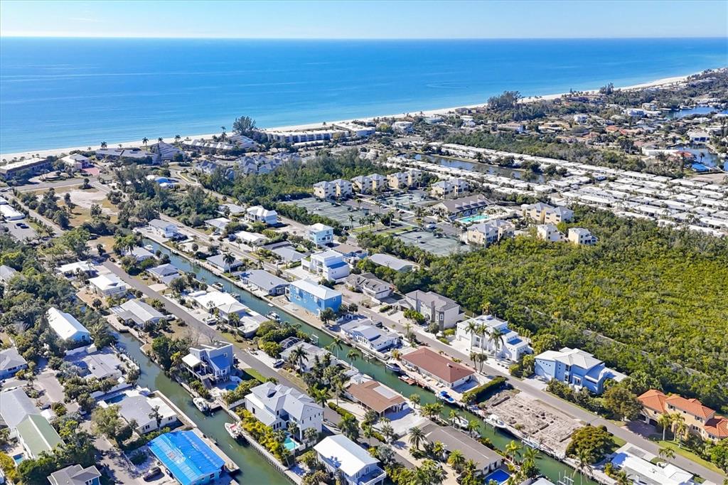 Aerial view of a coastal neighborhood with houses lining canals leading toward the beach — 651 JUNGLE QUEEN WAY, LONGBOAT KEY, FL