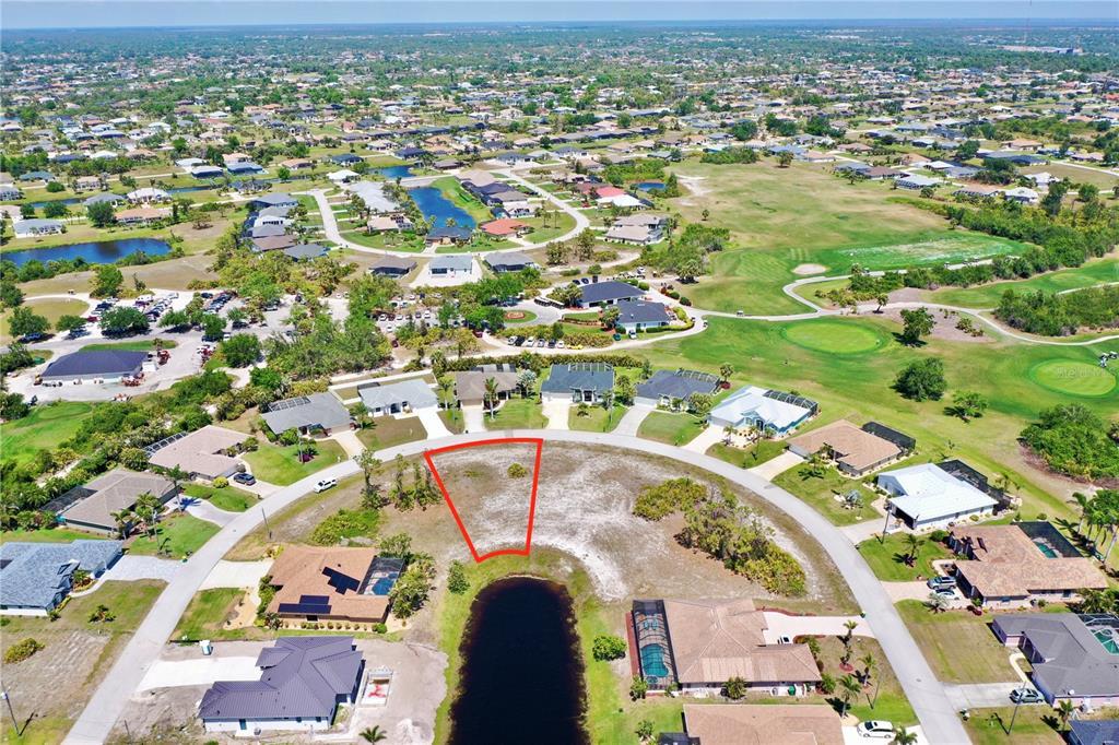 An aerial view shows a vacant, trapezoidal residential lot situated along a curved street and pond — 15 MEDALIST WAY, ROTONDA WEST, FL