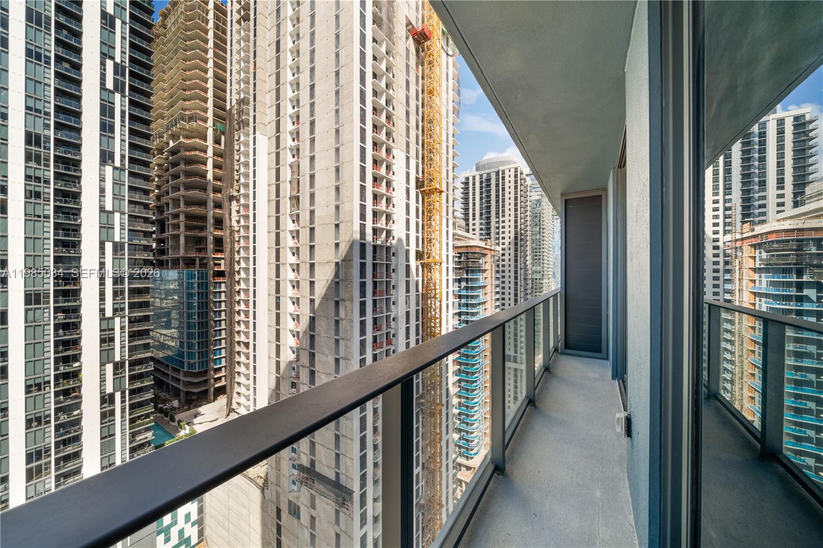 A balcony with a glass railing overlooks several tall high-rise buildings under construction — 121 NE 5th St # 2706, Miami FL 33132, MIAMI, FL