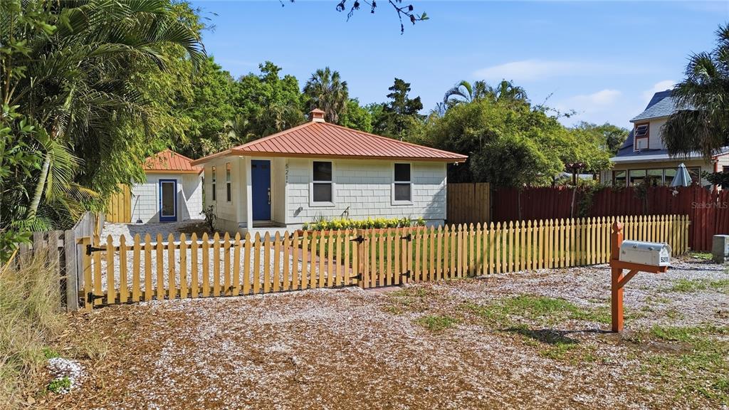 A small, light-colored house with a red metal roof sits behind a wooden picket fence — 5211 25TH AVENUE S, GULFPORT, FL