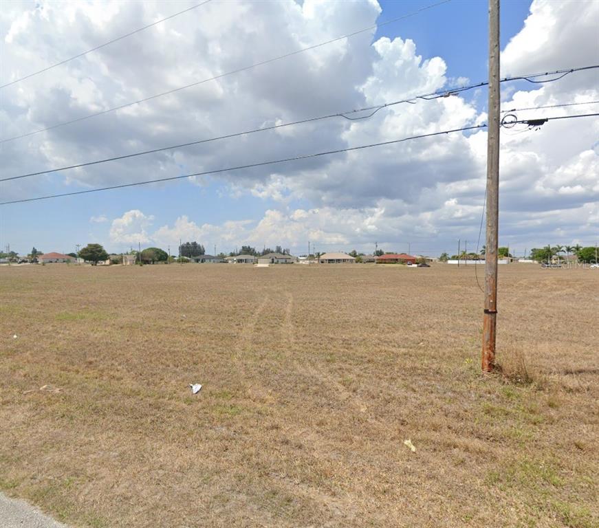A large, flat, grassy vacant lot is shown under a cloudy blue sky — 623 NE 15TH TERRACE, CAPE CORAL, FL