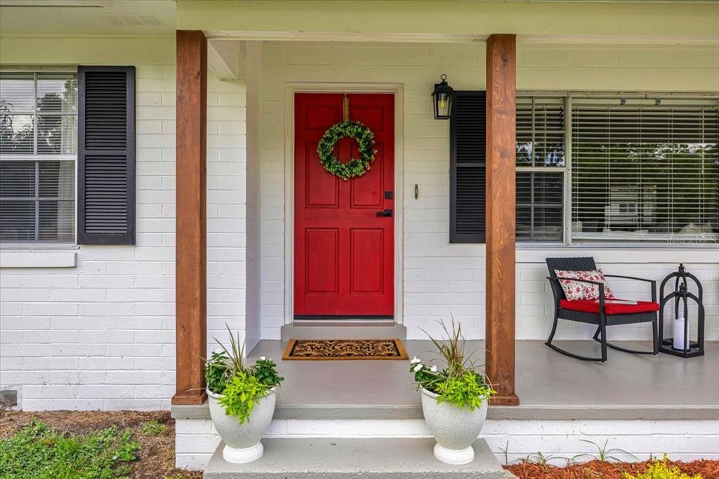 A red front door with a wreath sits between two wooden porch posts — 912 NE 17TH COURT, OCALA, FL