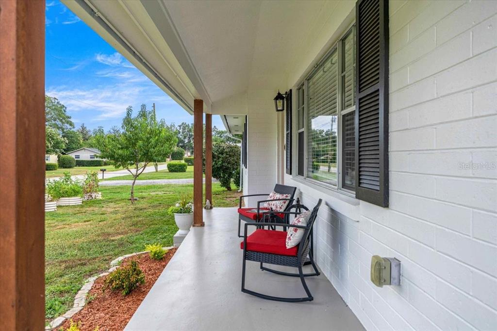 A covered porch features two rocking chairs with red cushions against a white brick wall — 912 NE 17TH COURT, OCALA, FL
