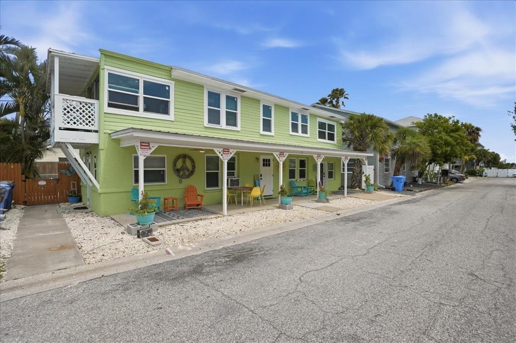 A two-story, light green building with a covered porch and outdoor seating sits along a street — 130 86TH TERRACE, TREASURE ISLAND, FL