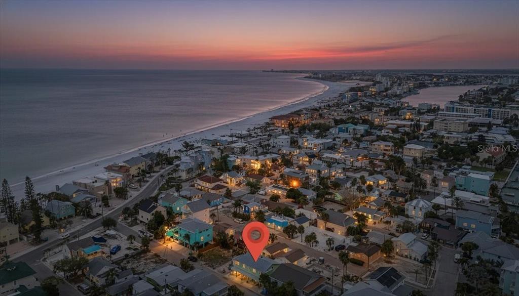 An aerial view shows a beach town at sunset with a red pin marking a house — 130 86TH TERRACE, TREASURE ISLAND, FL