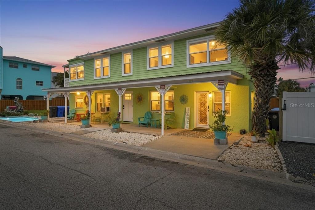 A two-story light green house with a covered porch, outdoor seating, and a small pool — 130 86TH TERRACE, TREASURE ISLAND, FL