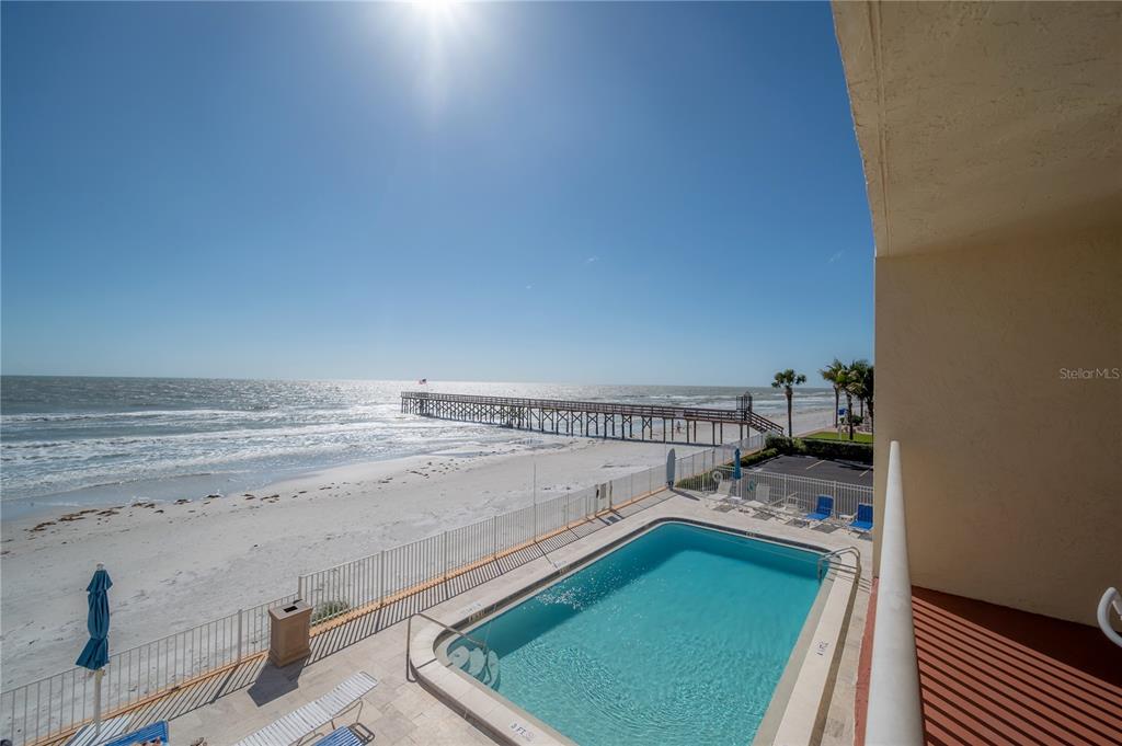 A balcony view overlooking a swimming pool, sandy beach, and a long wooden pier — 16308 GULF BOULEVARD UNIT 209, REDINGTON BEACH, FL