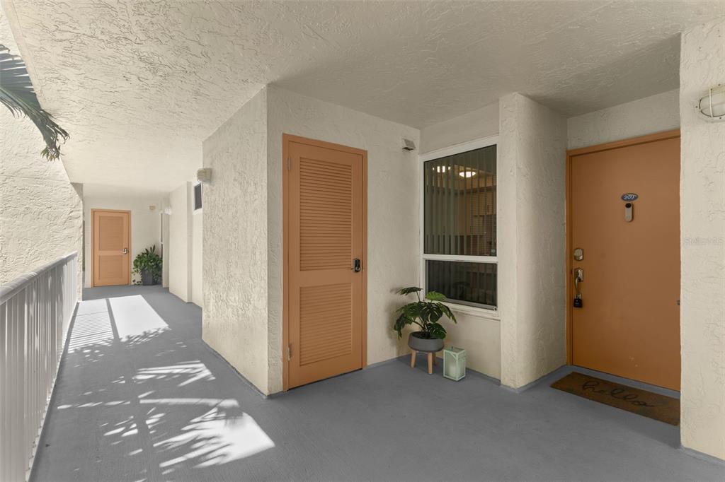 An outdoor apartment hallway features a tan door, a louvered utility closet, and a window — 16308 GULF BOULEVARD UNIT 209, REDINGTON BEACH, FL