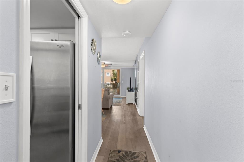 A hallway with wood-look flooring leads from a kitchen area toward a living room — 16308 GULF BOULEVARD UNIT 209, REDINGTON BEACH, FL