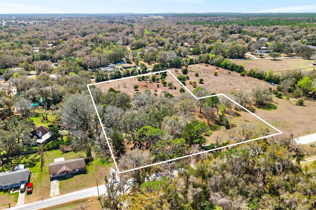 An aerial view shows a vacant, partially wooded lot outlined in white near a road — 7610 E SPANISH TRAIL, FLORAL CITY, FL