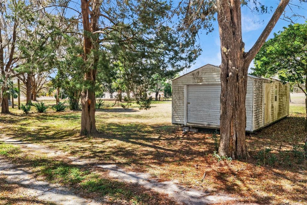 A white shed sits on a grassy lot surrounded by several large trees — 7610 E SPANISH TRAIL, FLORAL CITY, FL
