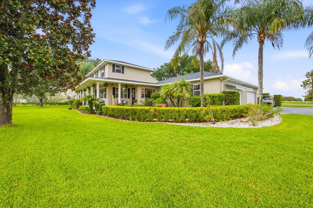 A two-story house with beige siding, a wrap-around porch, and palm trees on a lawn — 915 N CROOKED LAKE DRIVE, BABSON PARK, FL