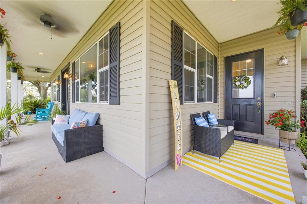 A covered porch features tan siding, a black front door, and outdoor seating areas — 915 N CROOKED LAKE DRIVE, BABSON PARK, FL