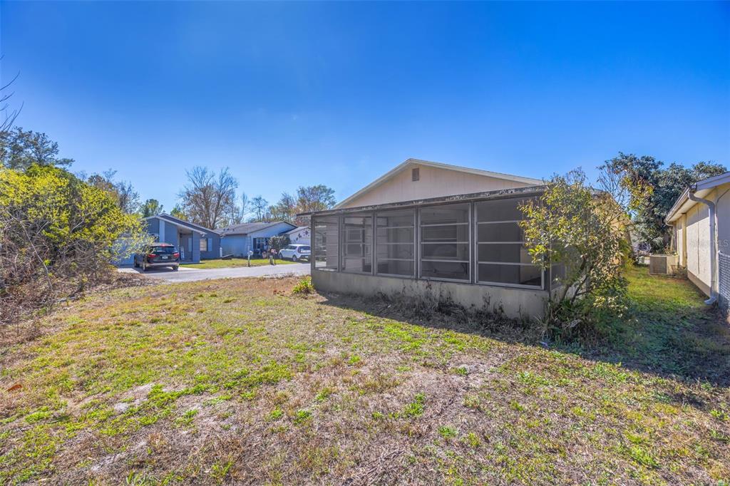 The exterior of a house features a large screened-in porch and a grassy backyard — 12622 TIMBERWOOD COURT, HUDSON, FL