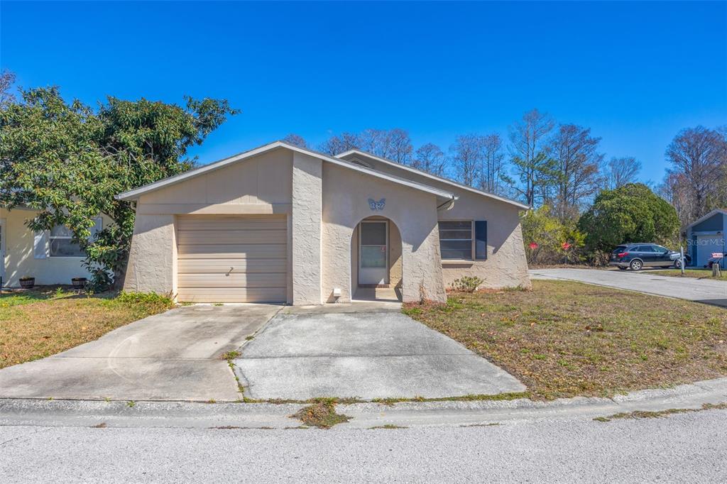 A single-story house with a beige stucco exterior, a one-car garage, and a concrete driveway — 12622 TIMBERWOOD COURT, HUDSON, FL