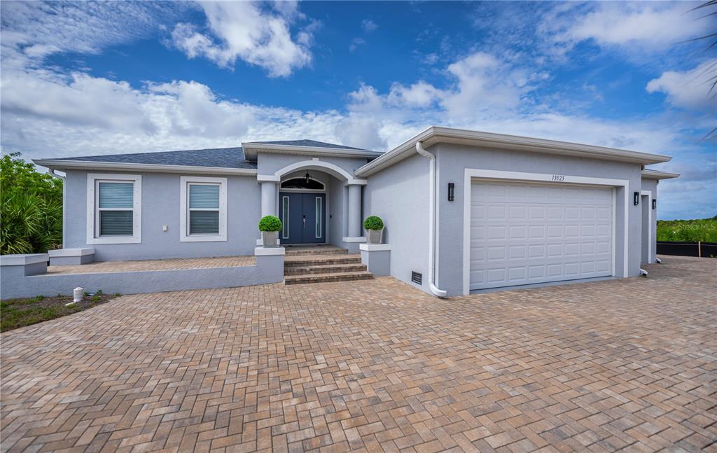 A single-story house with a gray stucco exterior, a paved driveway, and a two-car garage — 13525 GREENCASTLE AVENUE, PORT CHARLOTTE, FL