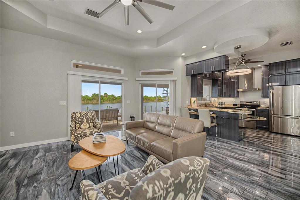 An open-concept living room and kitchen with gray marble-look tile floors and waterfront views — 13525 GREENCASTLE AVENUE, PORT CHARLOTTE, FL