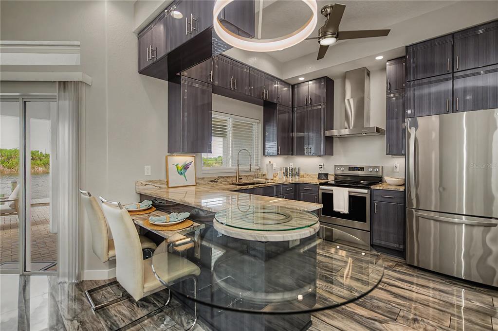 A modern kitchen features dark wood cabinetry, stainless steel appliances, and a glass-topped breakfast bar — 13525 GREENCASTLE AVENUE, PORT CHARLOTTE, FL