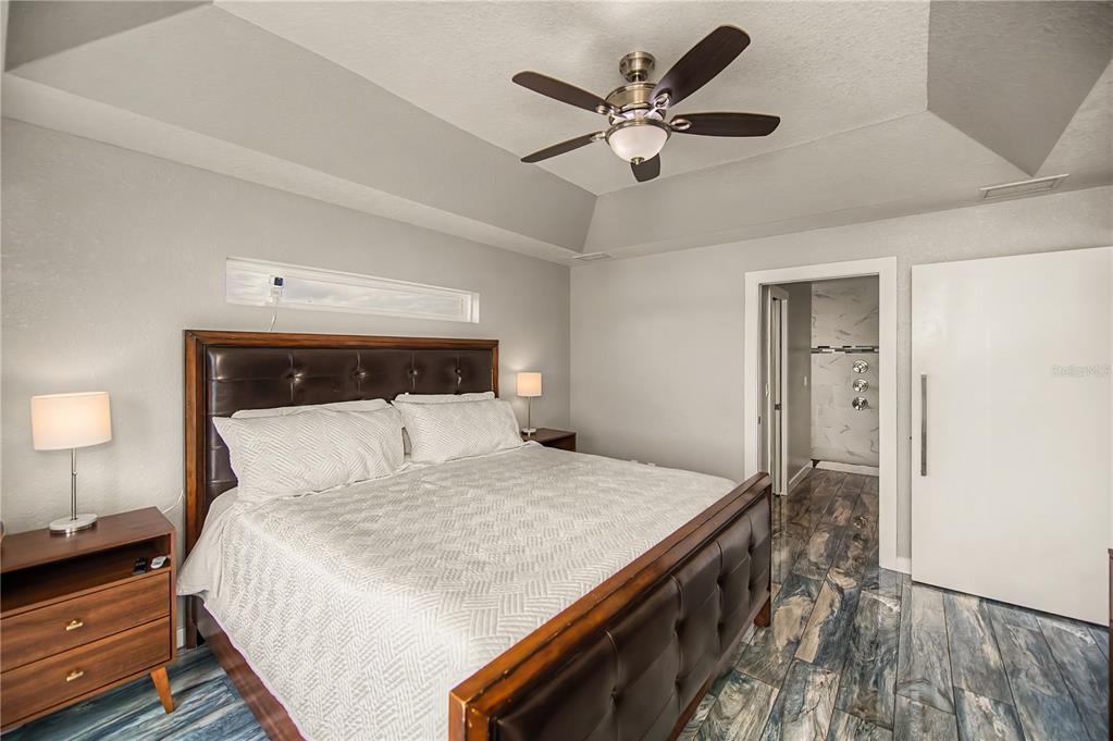 A bedroom features a tufted leather bed, wood-look tile flooring, and a ceiling fan — 13525 GREENCASTLE AVENUE, PORT CHARLOTTE, FL