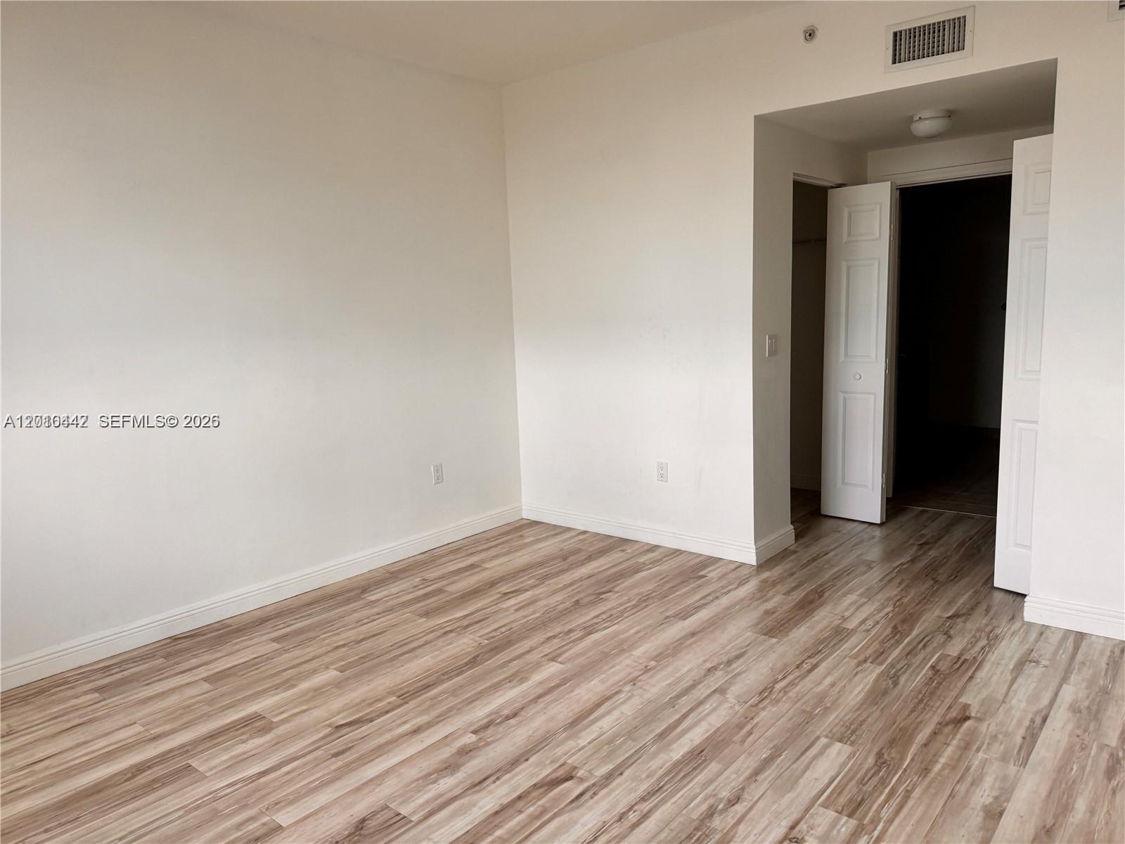 An empty room features light wood-look flooring, white walls, and an open closet doorway — 888 S Douglas Rd # 1602, Coral Gables FL 33134, CORAL GABLES, FL