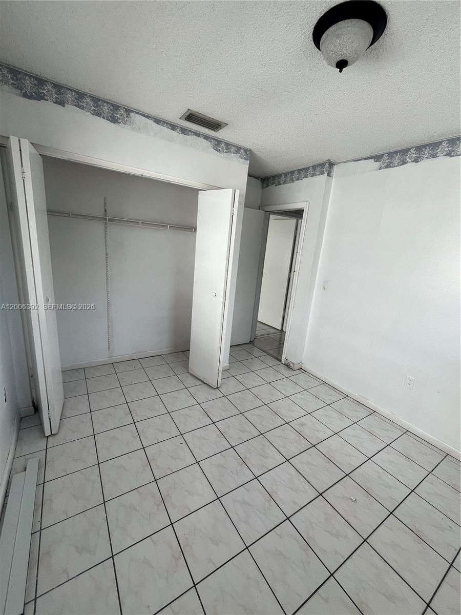 A bedroom features white tiled floors, a closet with open doors, and a doorway — 334 E 21st St # 5, Hialeah FL 33010, HIALEAH, FL