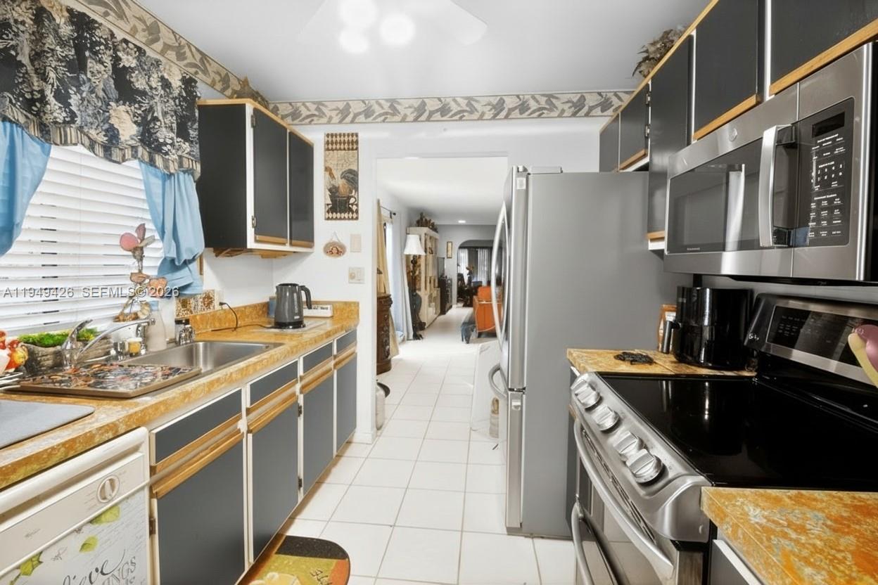 A galley kitchen features dark cabinets with wood trim, stainless steel appliances, and tiled flooring — 2214 Seagrape Cir, Coconut Creek FL 33066, COCONUT CREEK, FL
