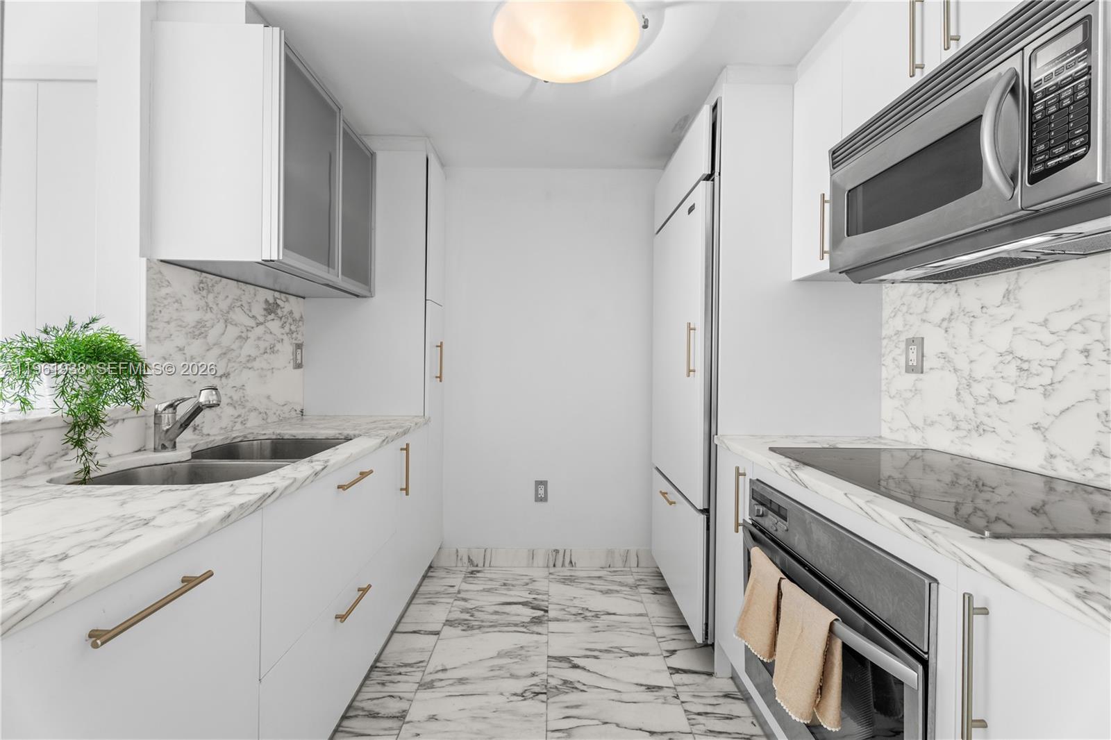 A galley kitchen features white cabinets, marble countertops, stainless steel appliances, and marble flooring — 450 Alton Rd # 3008, Miami Beach FL 33139, MIAMI BEACH, FL