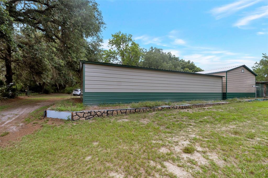 A long metal storage building with a stone-patterned retaining wall sits on a grassy lot — 2102 OLD POLK CITY ROAD, LAKELAND, FL