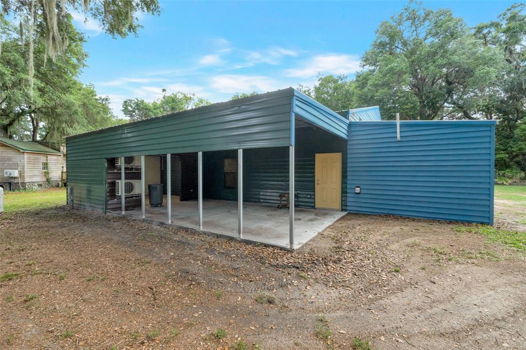 A metal-sided structure features a large open-air carport area and a single yellow door — 2102 OLD POLK CITY ROAD, LAKELAND, FL
